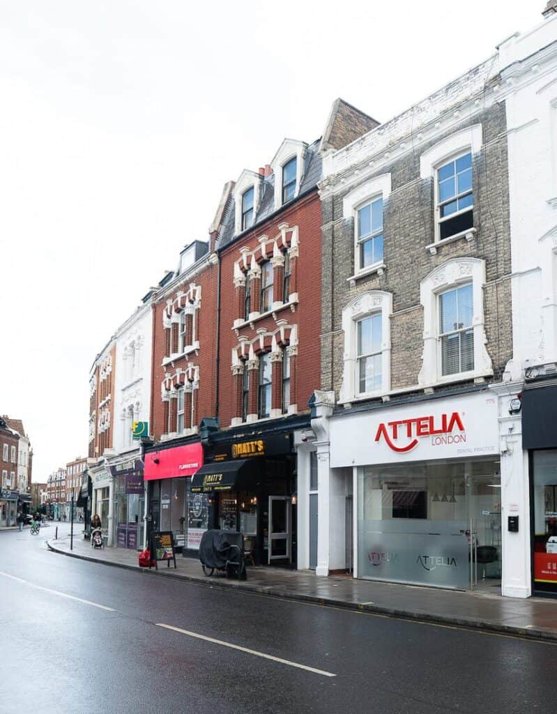 Attelia London storefront on a busy street with retail shops and historic buildings.