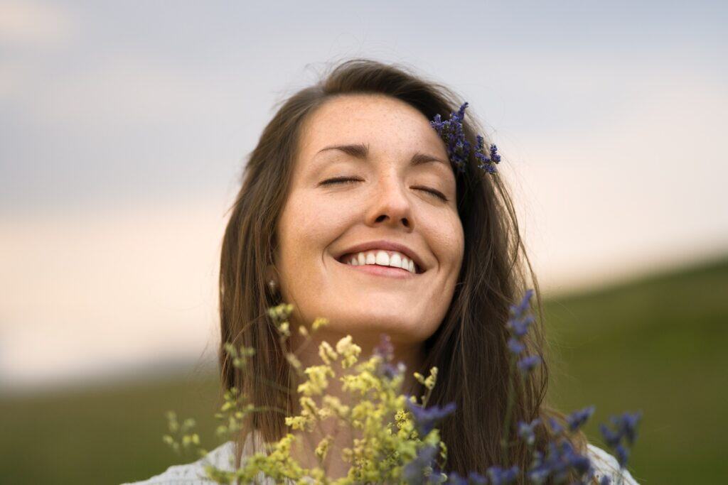 Woman smiling outdoors with flowers, promoting cosmetic dental options like bonding and veneers.
